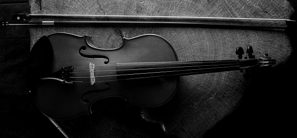 Old and beautiful violin on a rustic wooden surface and black background low key portrait, selective focus.