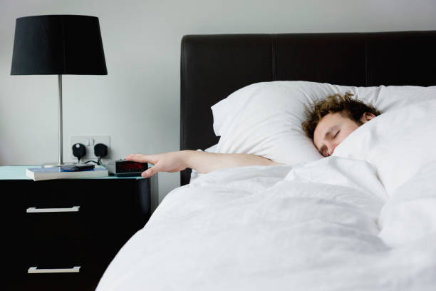 istock Man holding hand on alarm clock lying in bed 1273883712