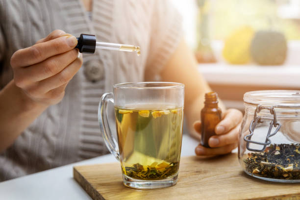 dietary supplements and vitamins - woman adding drop of cbd oil in cup of tea with pipette. anti stress dietary supplements and vitamins - woman adding drop of cbd oil in cup of tea with pipette. anti stress cbd oil photos stock pictures, royalty-free photos & images