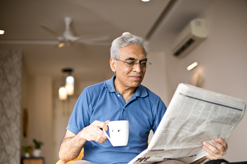 Senior man drinking coffee and reading newspaper at home