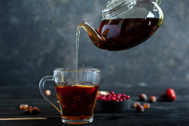 istock Hot black tea pours from a glass kettle into a cup on a dark background. 1273897466