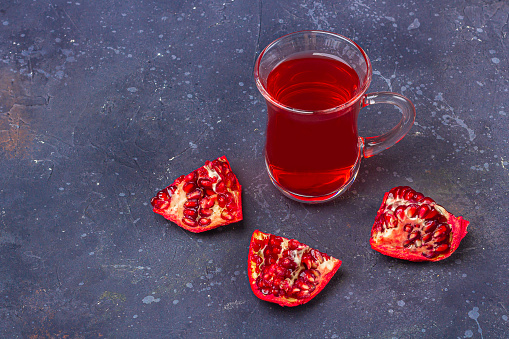 Red tea (rooibos, hibiscus, karkade) in Turkish tea cup (armudu) with  pomegranate in oriental style on dark background. Herbal, vitamin, detox tea for cold and flu. Copy space for text