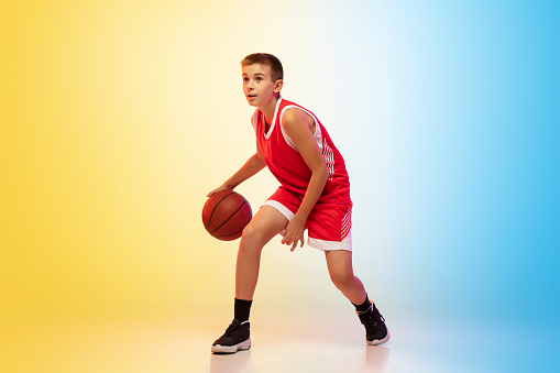 Strategy. Full length portrait of young basketball player in uniform on gradient studio background. Teenager confident posing with ball. Concept of sport, movement, healthy lifestyle, ad, action, motion.