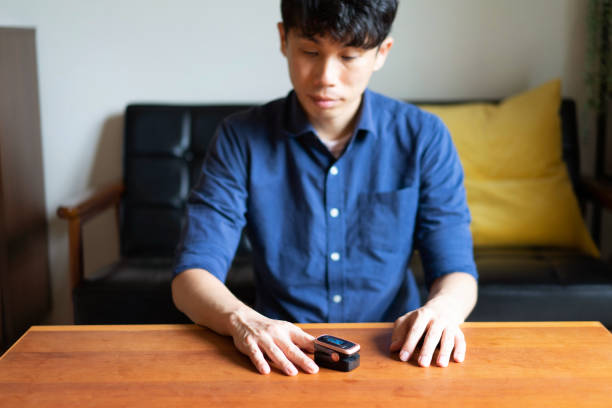 A man uses a pulse oximeter to measure the oxygen level in his blood A man uses a pulse oximeter to measure the oxygen level in his blood.
The pulse oximeter is pinching a human finger.
Home in the daytime. Living room. Solid wooden table.
Asian man. Taken in Japan. oxygen monitor stock pictures, royalty-free photos & images