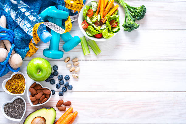 スポーツと健康的な食品の背景:果物、野菜、ナッツ、ダンベルとテープメジャー。スペースをコピーする - nut directly above multi colored food ストックフォトと画像