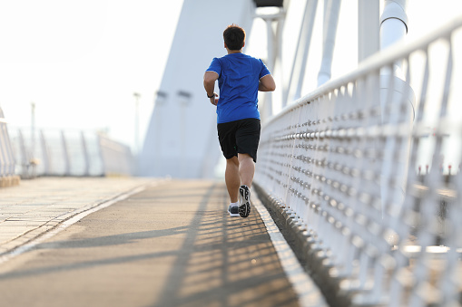 Rear view of obese man jogging on bridge for exercise with bridge background in the morning