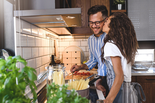 Young cheerful multi-ethnic couple preparing pasta together at their modern kitchen