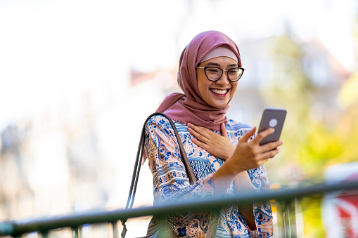Portrait of confident young woman wearing hijab standing with mobile phone outdoors