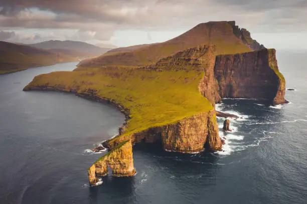 Famous Drangarnir Rock Formation in the North Atlantic Ocean in warm golden sunset light. Aerial Drone Point of view of the iconic Drangarnir Rock Formation between the Islet Tindholmur and Vágar Island, Faroe Islands, Denmark, Nordic Countries, Europe