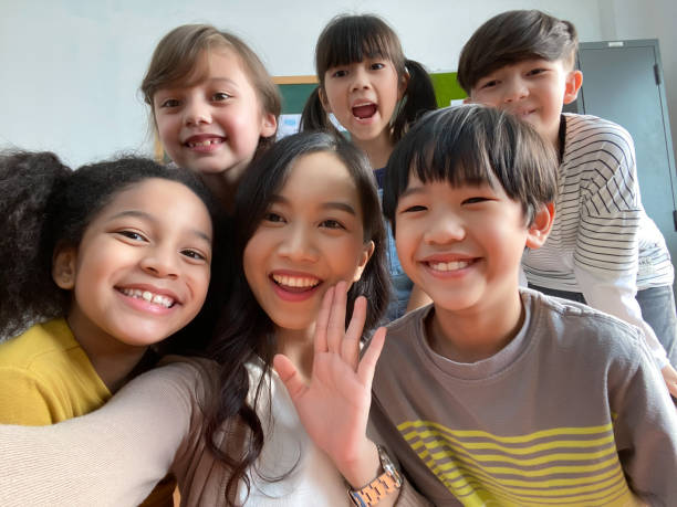 istock Smiling young Asian teacher making selfie with her schoolchildren in classroom. Elementary school,technology, children and people concept 1273919134