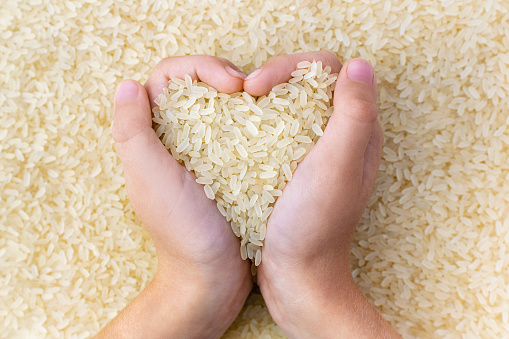 A child's hands hold a pile of dry white golden rice in a heart shape. Light grains of cereals, top view. Organic natural food, health care. An ingredient for traditional Asian cuisine.