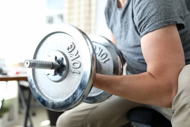 guy sits at home and lifts heavy metal dumbbells - muscle build imagens e fotografias de stock