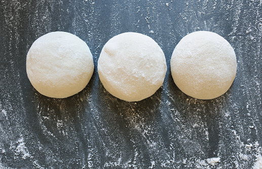 Three balls of fresh homemade wheat dough on kitchen table. Home baking. Dough for pizza cooking, pasta dumplings or bread.Horizontal.