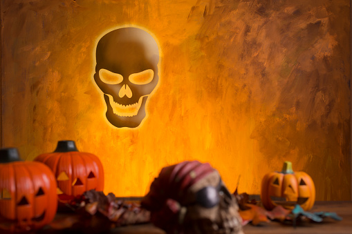 Bright orange background appears as to be an inferno with Halloween decorations in foreground and in the blazes in background.  Skull appears in background.
