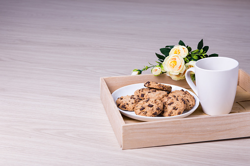 tray with chocolate chip cookies, tea and flowers on wooden table background