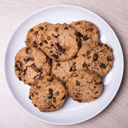 top view of chocolate chip cookies on white plate on wooden table background