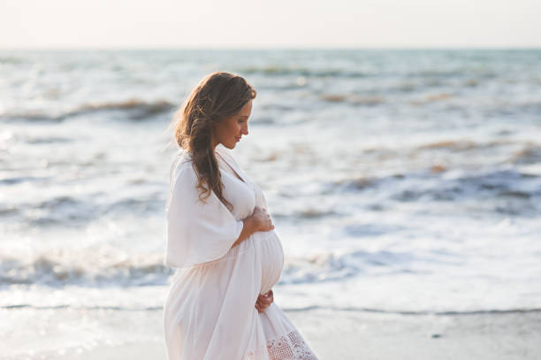 pregnant woman at beach - dress human pregnancy young women women imagens e fotografias de stock