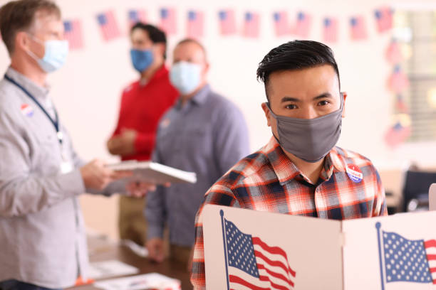istock Asian descent man votes in USA election wearing mask. 1273942172