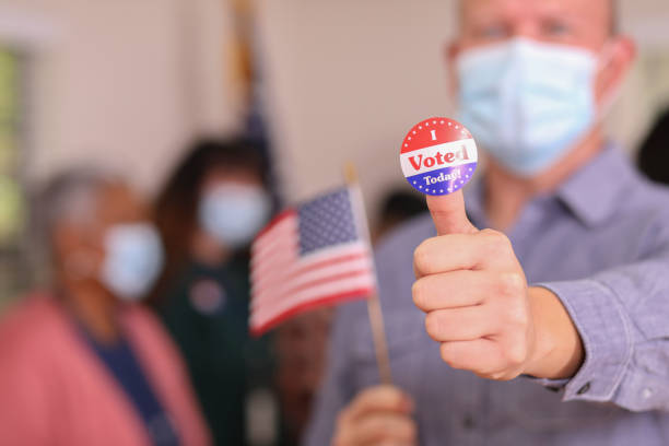 istock Man votes in USA election wearing mask and I Voted sticker. 1273942349
