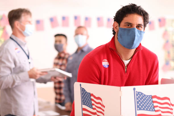 istock Latin descent man votes in USA election wearing mask. 1273943524
