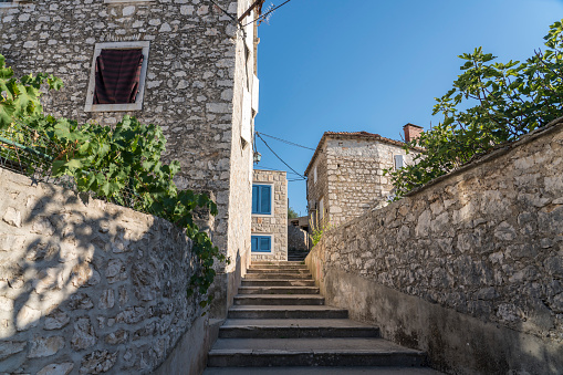 Stone stairs going up the street, stone facades of old houses against blue sky.