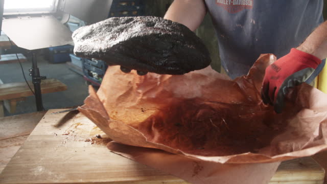 Man Unwrapping a freshly smoked and  Barbecued Beef Brisket onto a rustic wooden cutting board ready to be sliced and served