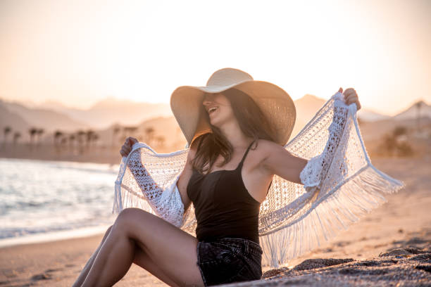 istock Beautiful boho model in a hat poses on the beach in the sun 1273995896