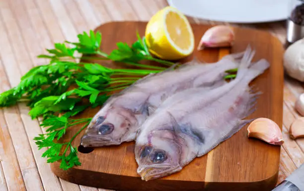 Uncooked roosterfish with greens and garlic on wooden board before cooking