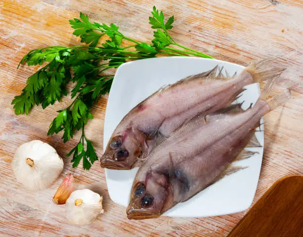 Uncooked roosterfish with greens and garlic on wooden board before cooking