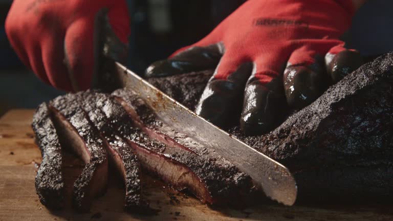 Gloved Hands Slowly Cutting Perfectly Cooked Texas Barbecue Style Beef Brisket on a Rustic Cutting Board