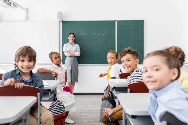 istock teacher with crossed arms and multicultural pupils looking at camera during lesson 1274064355
