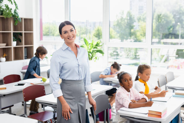 istock teacher looking at camera while standing in classroom near multicultural pupils 1274064450