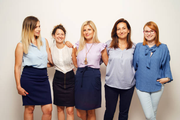 istock Five women standing on front of white wall looking to the camera smile as a team - Front view group of people indoor studio shot business concept 1274084412