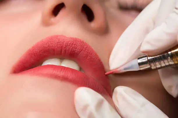 Permanent make up procedure, applying on young girl. Lip makeup in tattoo salon. Close up shoot.