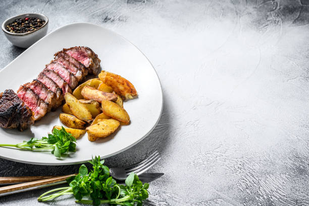 istock Sliced striploin steak with potato. White background. Top view. Copy space 1274096151