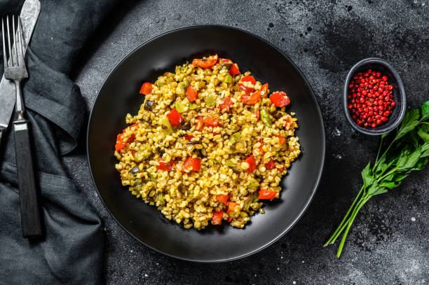 Bulgur with vegetables, onions, sweet peppers, carrots and parsley in a plate. Black background. Top view Bulgur with vegetables, onions, sweet peppers, carrots and parsley in a plate. Black background. Top view. bulgur wheat stock pictures, royalty-free photos & images