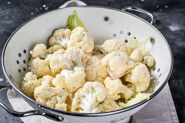 Washed fresh cauliflower cut into pieces in a colander. Black background. Top view