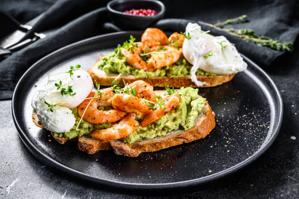 panino condito con gamberi freschi, gamberetti su avocado con uovo. un cibo sano, cucina scandinava. sfondo nero. visualizzazione dall'alto - sandwich avocado prepared shrimp bread foto e immagini stock