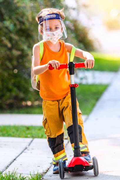 istock Serious urban schoolboy going back to school wearing a protective face mask and a face shield using a push scooter 1274262893