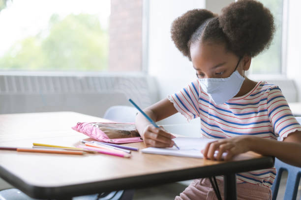 istock Elementary girl wearing a protective face mask working on school assignment 1274272694