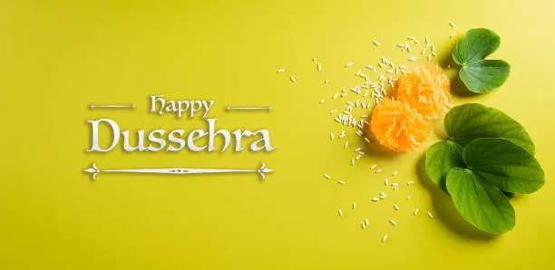 Happy Dussehra background concept. Green leaf and rice on yellow pastel background. Dussehra Indian Festival concept.