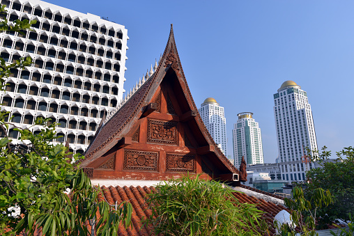 Old, wooden temple of Buddha against contemporary architecture in central Bangkok, Thailand.
