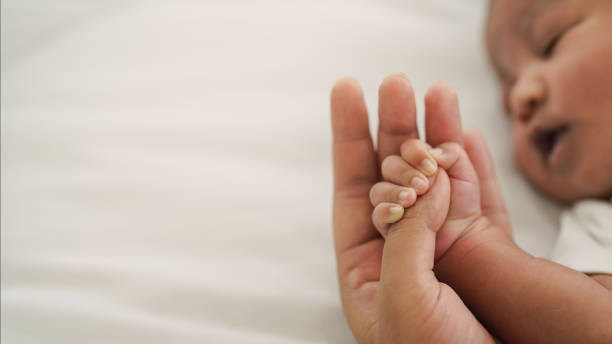 main de nouveau-né afro-américaine de nouveau-né retenant le doigt de maman sur le lit blanc - nouveau né photos et images de collection