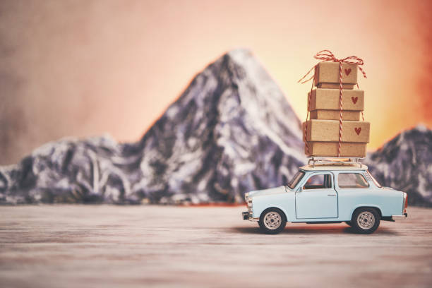 Little blue car with gift stack on roof rack in front of mountain range