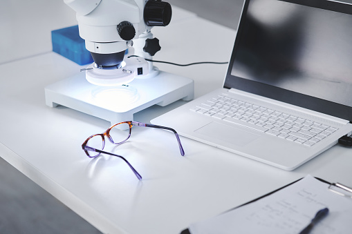 Closeup shot of spectacles on a desk alongside a laptop and microscope in a lab