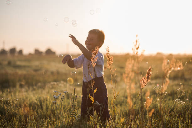 istock Boy blowing soap bubbles while an excited kid enjoys the bubbles. Happy kid in a meadow 1274473168