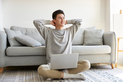 happy young asian business man staying at home sitting on carpet working using laptop computer happy and smiling