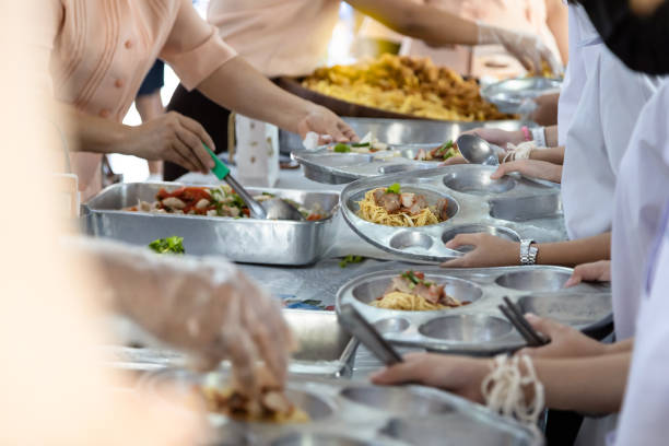 los maestros asiáticos están distribuyendo alimentos a los estudiantes, los estudiantes de la escuela primaria están esperando o haciendo cola para recibir comida gratis, niños durante el almuerzo, comer el almuerzo o la actividad escolar, de vuelta al - tray lunch education food fotografías e imágenes de stock