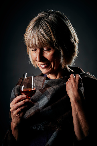 Confident mature woman wearing a plaid shawl relaxing with a glass of whisky.