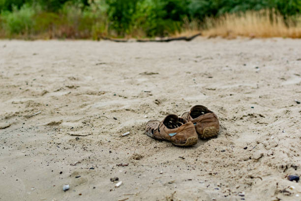 vieilles chaussures brunes usées, debout seules sur la plage de sable fin. chaussures piétinées pour hommes dans la nature sans - sandy brown photos photos et images de collection